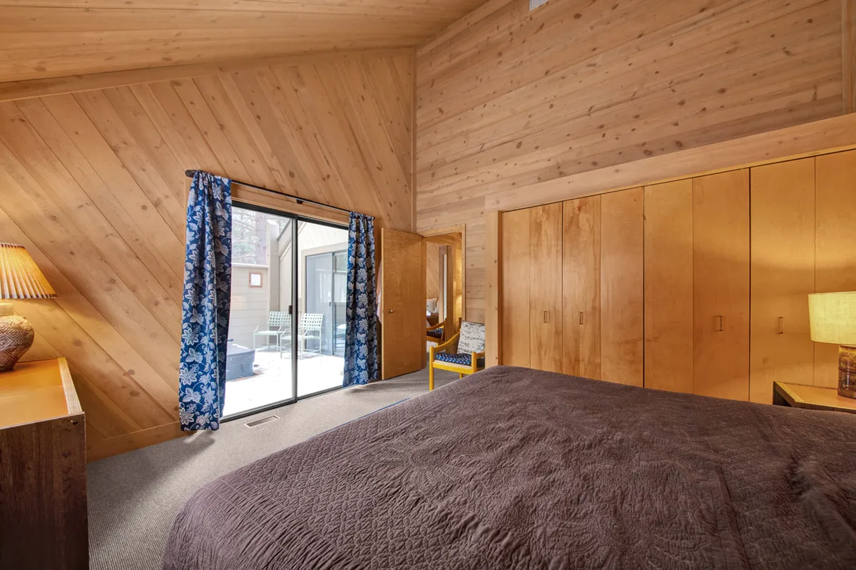 A tranquil bedroom scene with a large sliding glass door opening out to fresh air. The bed is dressed in a textured blanket, and colorful curtains frame the doorway, creating a warm and inviting atmosphere. The outdoor visibility highlights possibilities for pet-friendly play just outside.