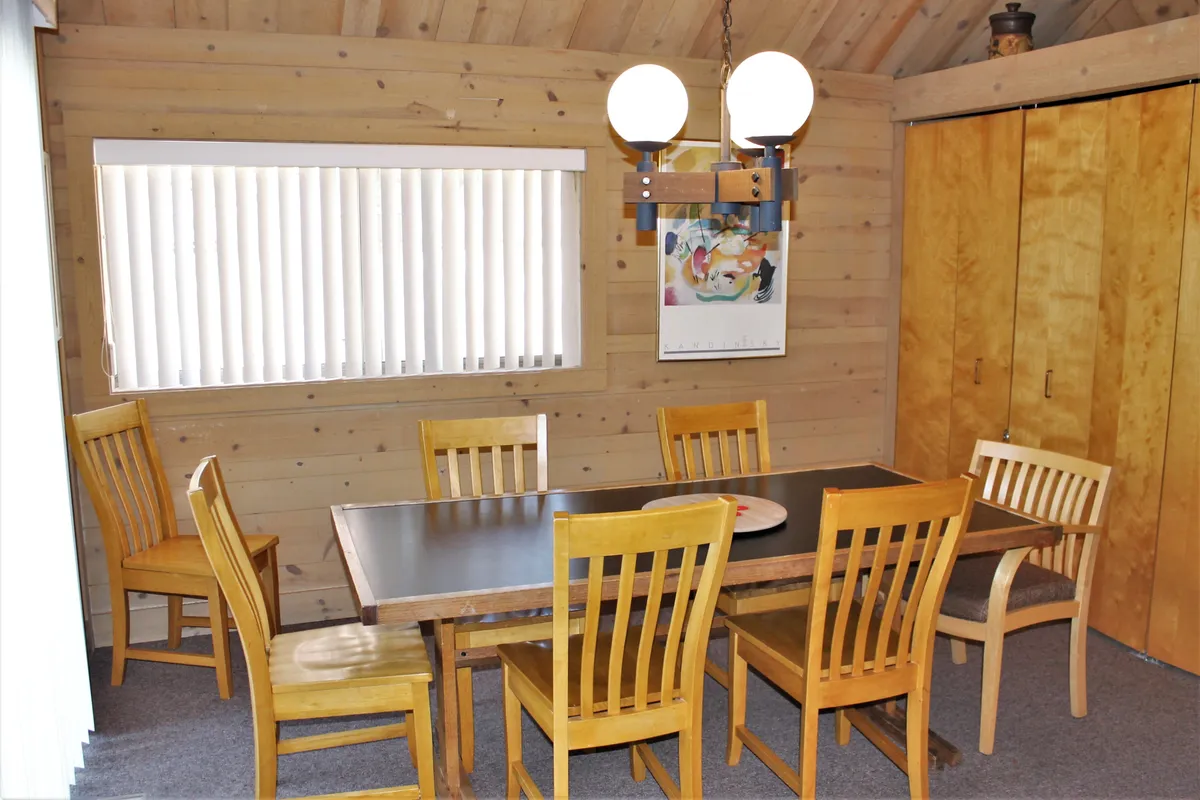 A warmly-lit dining area with a central table, surrounded by wooden walls and accented by a modern light fixture. The space radiates togetherness, ideal for family meals, games, and shared experiences.