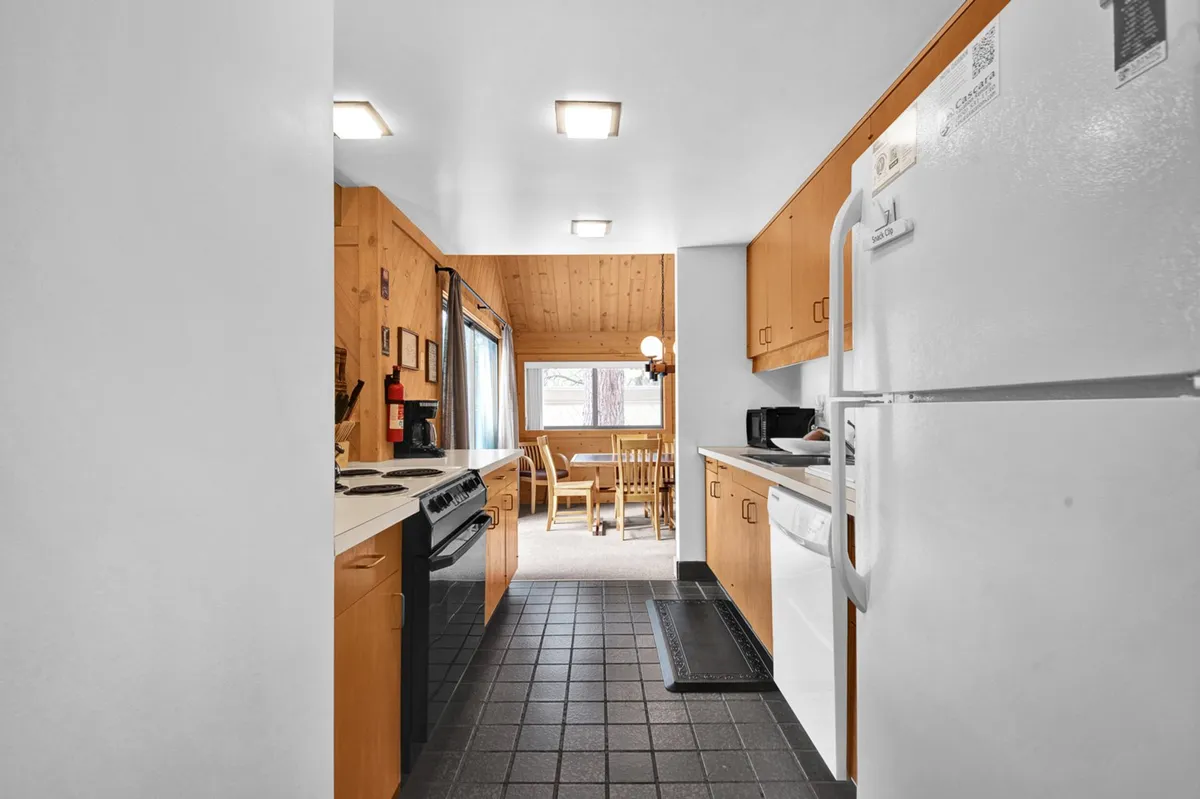 A view from the kitchen looking out to the dining area and a large window, with wooden cabinetry and modern appliances on display. The scene is bright and encourages togetherness, reflecting moments of cooking, baking, or sharing stories over a meal.