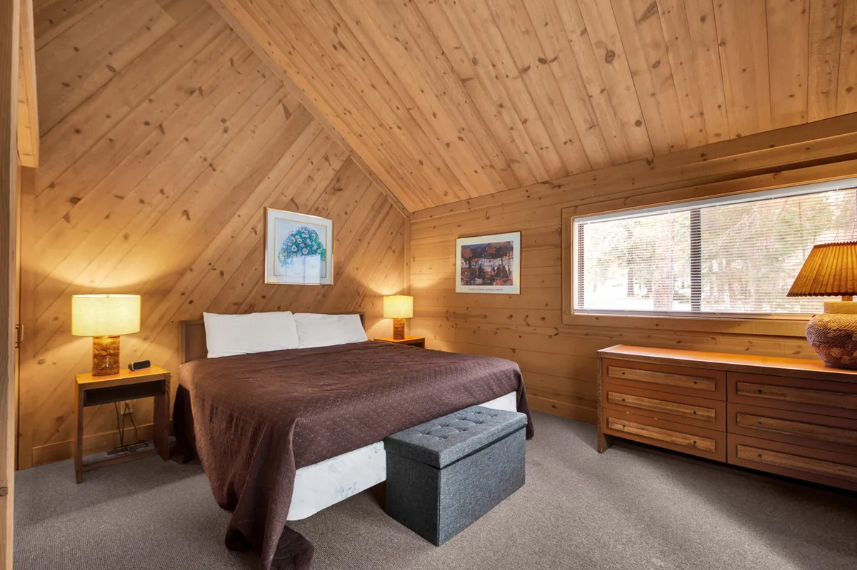 A cozy bedroom featuring a plush king-sized bed with a beautifully patterned quilt, matching nightstand lamps, a wooden chest at the foot of the bed, wall art adding a touch of personality, and a window letting in gentle natural light. The room exudes warmth and tranquility, making it ideal for restful sleep.