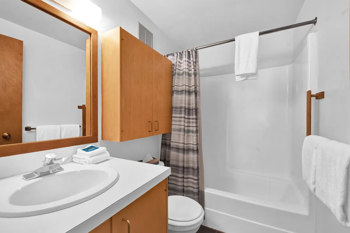 A view of a full bath with a vanity sink, mirror, wooden cabinets, and a shower curtain, all in a calm, practical setting. The bathroom is clean and accessible—ideal for families or groups staying in the loft.