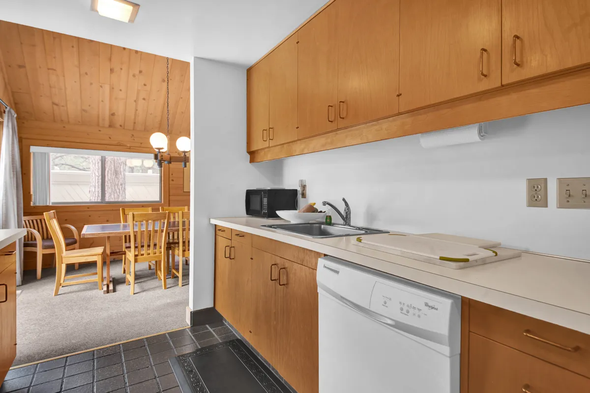A cozy kitchen and dining area highlighted by a prominent window, which provides a glimpse of the outdoor scenery. The space is set up for gatherings and casual meals, suggesting a communal atmosphere adjacent to the outdoor views.